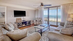 A living room with a sofa set, a glass coffee table, a TV, and a view of the ocean through a sliding glass door. - Oceanviews-MultiBalconies-Steps 2 Beach-Pool/HotTub-Gated Community-Kingston (Myrtle Beach)