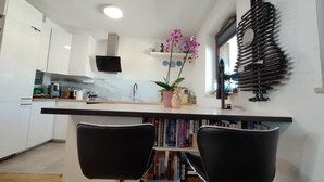 A modern kitchen with white cabinets, a black countertop, and a central island with chairs. There is a bookshelf with books and a potted plant. - Unique Apartment With Amazing 90 m² Roof Terrace (Wroclaw)