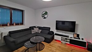 A modern living room with a sectional sofa, a coffee table, a flat-screen TV, and a decorative tree wall art piece. - Unique Apartment With Amazing 90 m² Roof Terrace (Wroclaw)