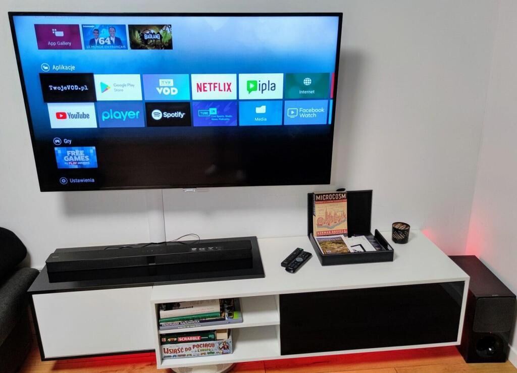 A flat-screen TV mounted on a white entertainment unit with a remote control, a book titled 'MICROCOSM,' and a small speaker.