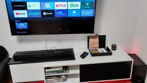 A flat-screen TV mounted on a white entertainment unit with a remote control, a book titled 'MICROCOSM', and a small speaker. - Unique Apartment With Amazing 90 m² Roof Terrace (Wroclaw)