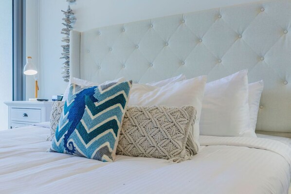 A neatly made bed with a tufted headboard, a bedside table with a lamp, and decorative wall art. - Relax at the Jacuzzi or ride to the sea from here (Noord)