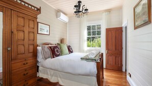 A bedroom with a wooden bed, a dresser, a chandelier, and a window with a view of greenery.