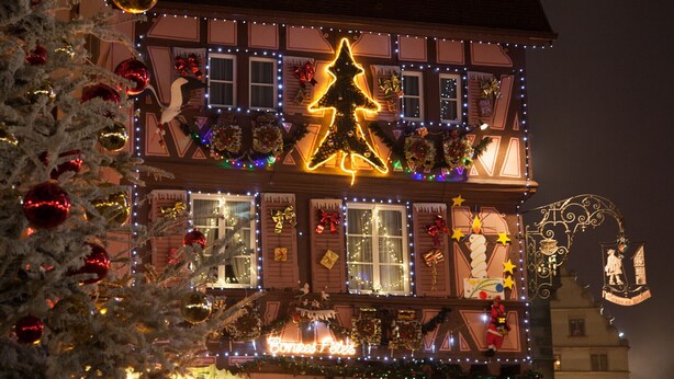 Un bâtiment européen traditionnel, agrémenté de guirlandes lumineuses et de décorations de Noël, notamment un grand sapin de Noël illuminé et des couronnes festives.