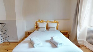 Un lit bien fait avec deux oreillers, une tête de lit en bois avec des lampes, une petite table de chevet en bois et un radiateur.