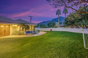 Una propiedad residencial con un césped cuidado, un patio con mobiliario exterior y montañas al fondo.