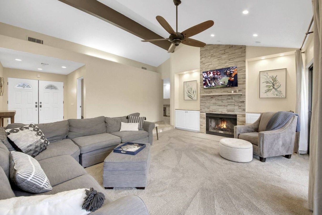 A spacious living room with a large gray sectional sofa, a fireplace, and a ceiling fan.
