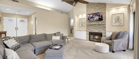 A spacious living room with a large gray sectional sofa, a fireplace, and a ceiling fan.