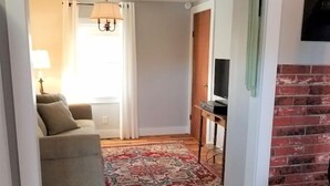 A hallway leading to a living room with a sofa, a TV, and a patterned rug.