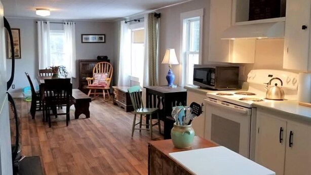 A spacious living area with a wooden floor, a dining table, and a kitchen area with a microwave and stove.