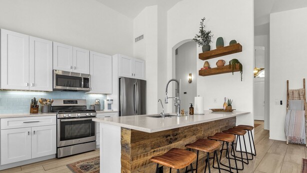 A modern kitchen with white cabinets, stainless steel appliances, and a central island with bar stools. - Incredible golf course views with modern, southwest inspired decor (Mesa)