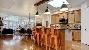 A spacious kitchen with wooden cabinets, a central island with bar stools, and pendant lighting. - Mistaya Suite | Stylish Downtown Penthouse (Canmore)