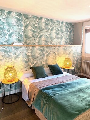 A bedroom with a bed, two bedside lamps, a window, and a radiator.