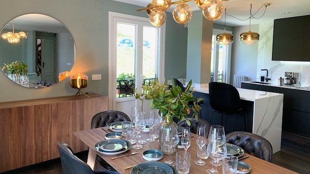 A dining area with a wooden table set for a meal, a mirror, and a modern kitchen in the background. - Exclusive housing in the center of Burgos. (Burgos)