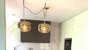 A modern kitchen with a central island, two bar stools, pendant lighting, and built-in appliances. - Exclusive housing in the center of Burgos. (Burgos)