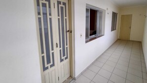 A hallway with a large beige door with glass panels, a window with blinds, and a plain tiled floor.