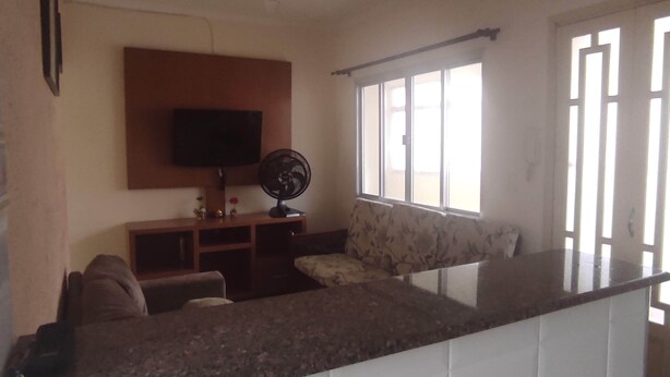 A living room with a flat-screen TV mounted on the wall, a standing fan, and a sofa.