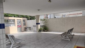 A covered outdoor area with tiled flooring, two benches, and potted plants.
