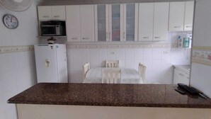 A compact kitchen with white cabinets, a microwave, a refrigerator, and a dining table with chairs.