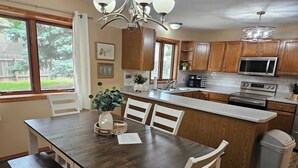 A kitchen with wooden cabinets, a stainless steel microwave, an oven, and a sink. There is a dining table with chairs and a vase with flowers.