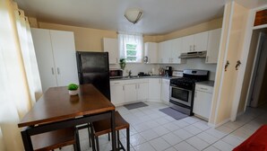 Una cocina compacta con armarios blancos, un refrigerador negro, una estufa y un comedor con una mesa y sillas de madera.