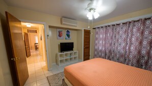 Un dormitorio con cama, televisión, armario y ventilador de techo.