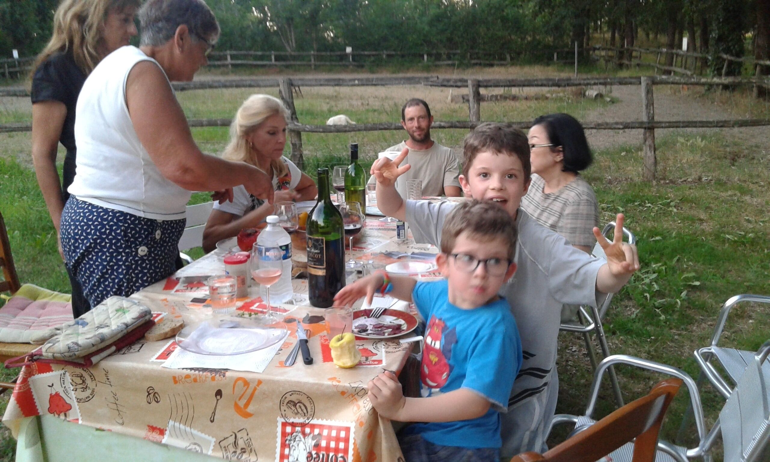 Un groupe de personnes est assis autour d’une table recouverte d’une nappe, avec des assiettes et des bouteilles.