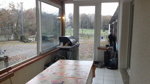 Een kamer met uitzicht op een omheind buitengebied, een barbecue en een ventilator bij het raam.