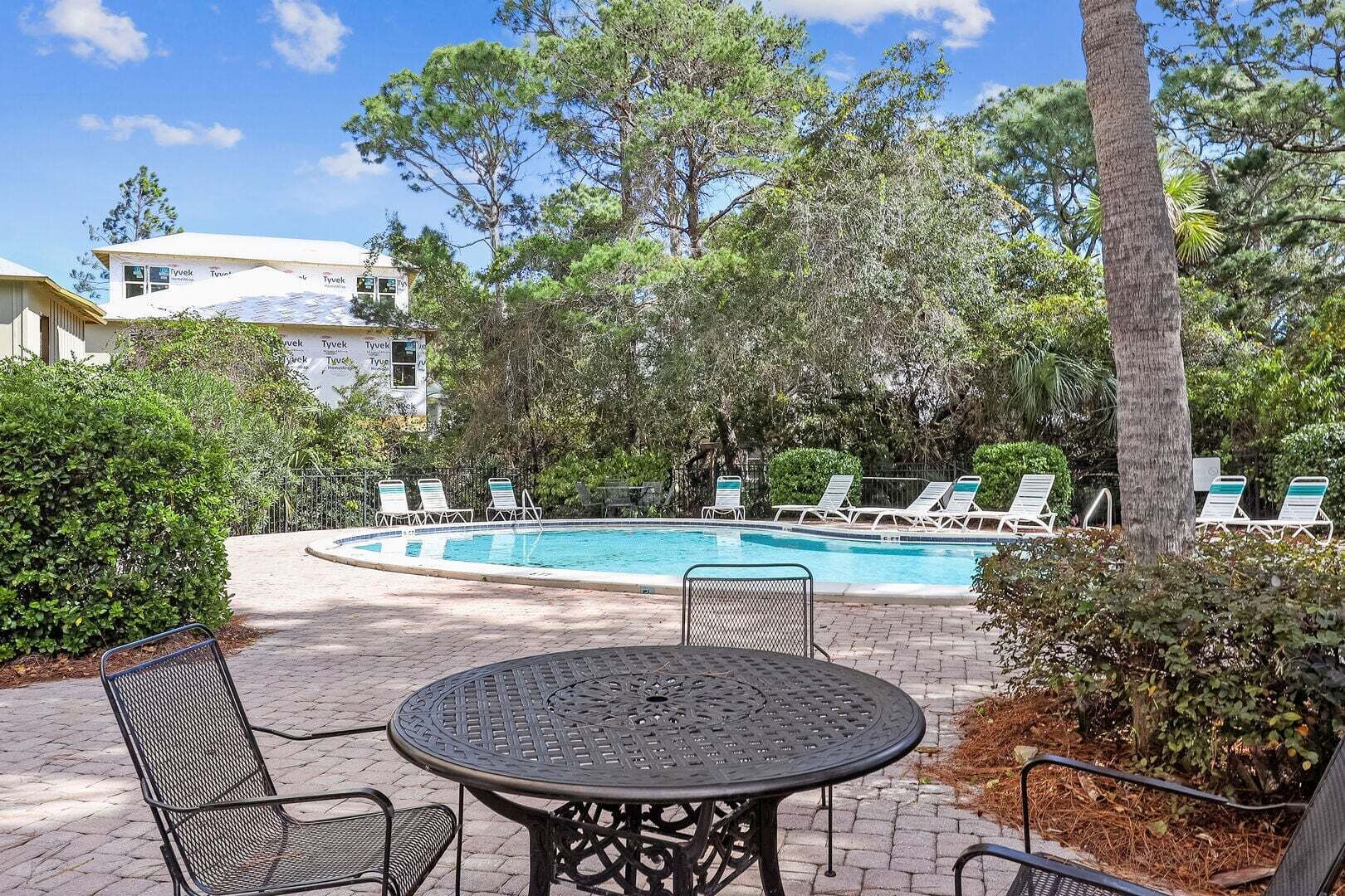 Un espace piscine avec des chaises longues, une table et un bâtiment en arrière-plan.