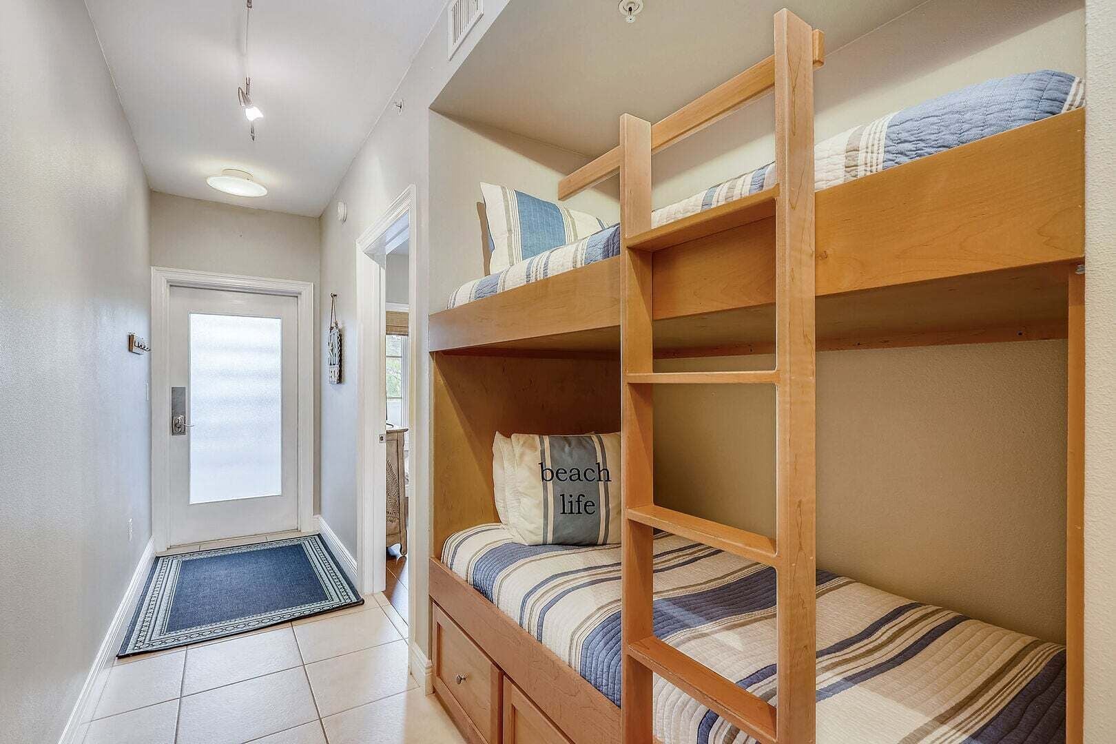 Une chambre avec un lit superposé, une porte, un petit tapis et un luminaire.
