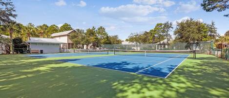 A tennis court with a net, surrounded by trees and a building.