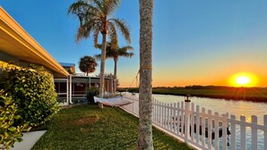 A waterfront property with a hammock, palm trees, and a white fence. - Oasis on the Gulf, screened pool, sunset, kayaks! (Hernando Beach)