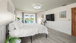 A bedroom with a bed, a TV, and a view of a pool. - Oasis on the Gulf, screened pool, sunset, kayaks! (Hernando Beach)