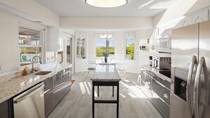 A modern kitchen with a central island, stainless steel appliances, and large windows offering a view. - Oasis on the Gulf, screened pool, sunset, kayaks! (Hernando Beach)