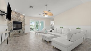A spacious living room with a stone fireplace, a flat-screen TV, a ceiling fan, and a large sectional sofa. - Oasis on the Gulf, screened pool, sunset, kayaks! (Hernando Beach)