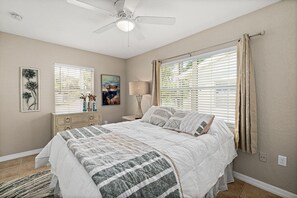 A bedroom with a bed, a ceiling fan, a nightstand, a lamp, and a window with blinds.