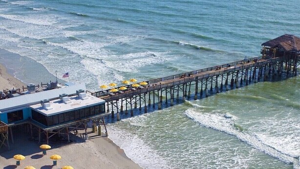 A beach with yellow umbrellas and a pier extending into the ocean. - Hidden gem just a drive from the beach and village (Merritt Island)