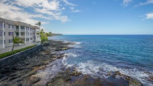 A coastal hotel with a rocky shoreline, ocean view, and a clear sky. - Hale Kona Kai 312 - Absolute Oceanfront Condo with wraparound lanai (Kailua Kona)