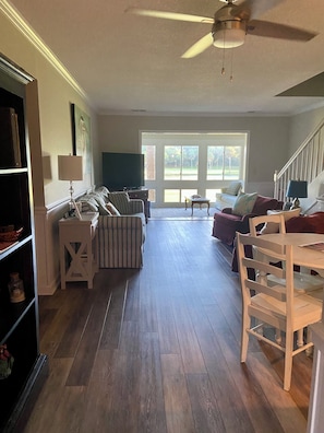 Ein geräumiges Wohnzimmer mit großem Fenster, Deckenventilator und Essbereich mit Tisch und Stühlen.