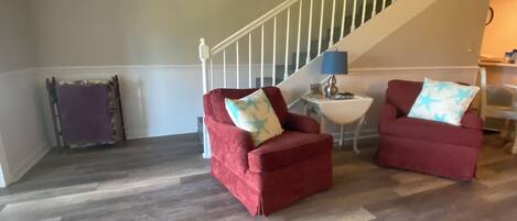 A living room with two red armchairs, a small white side table with a lamp, and a staircase in the background.