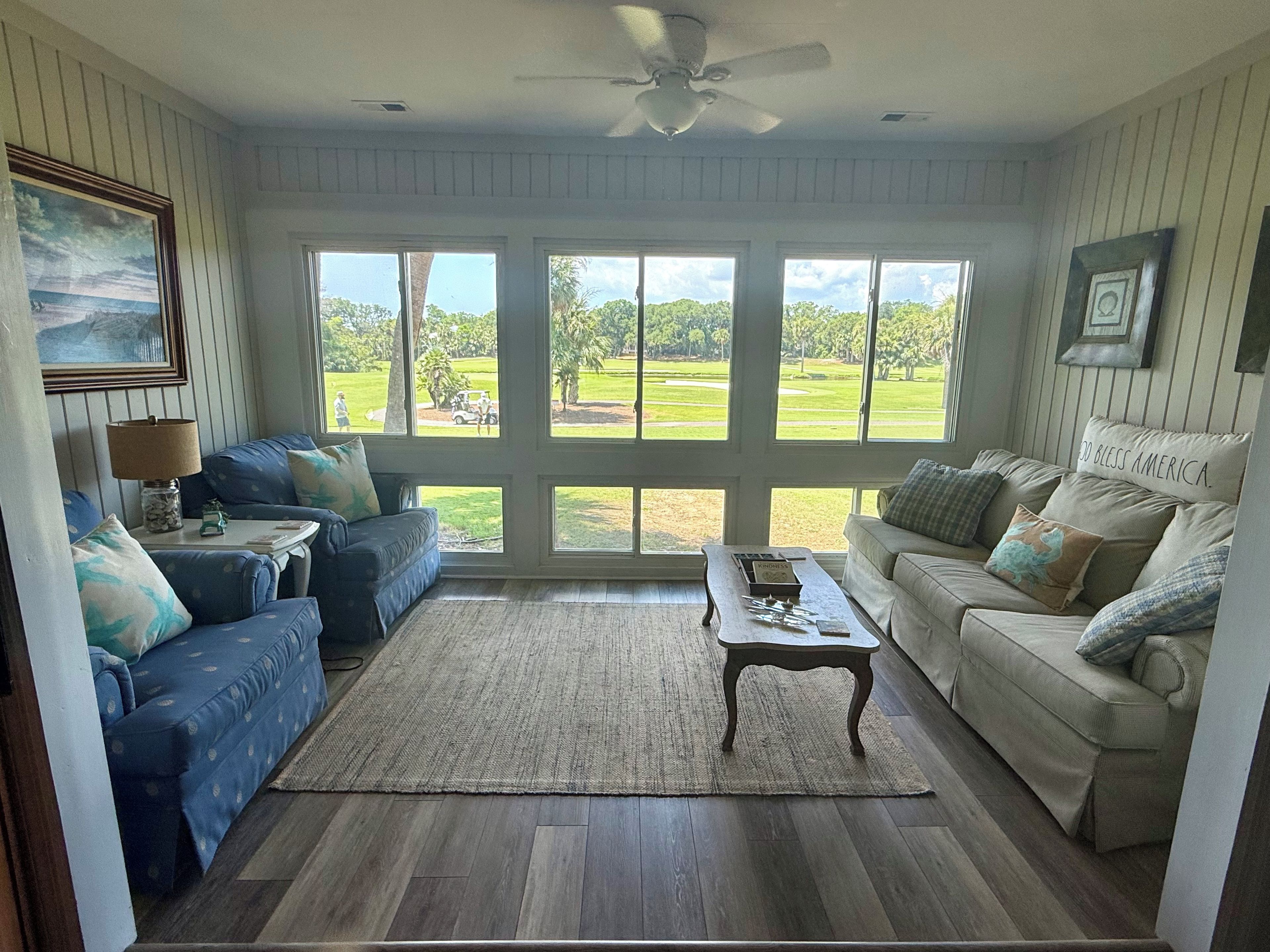 A living room with a large window, a ceiling fan, and two sofas.