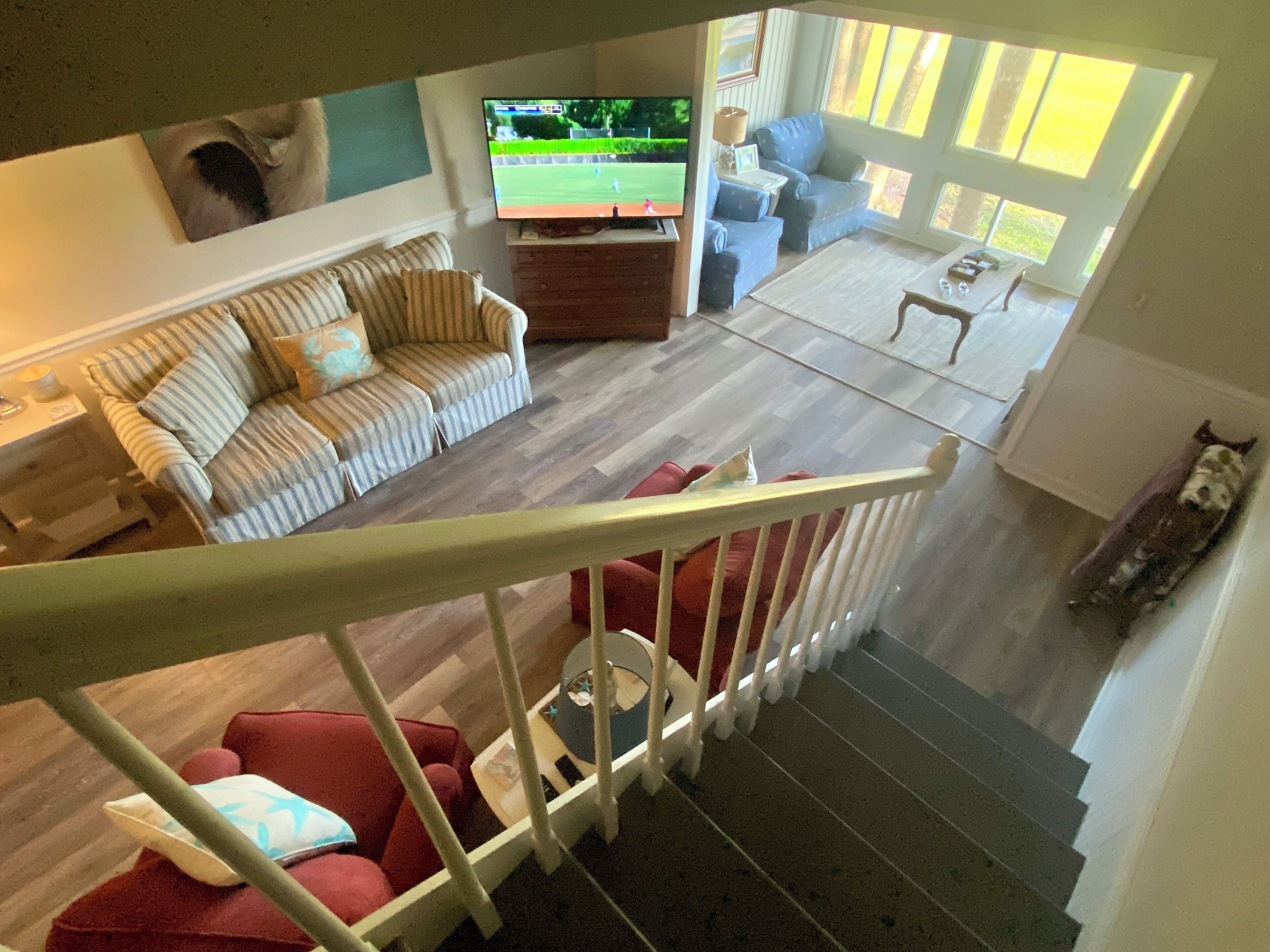 A spacious living area with a large flat-screen TV, a striped sofa, a red armchair, and a staircase leading to an upper level.