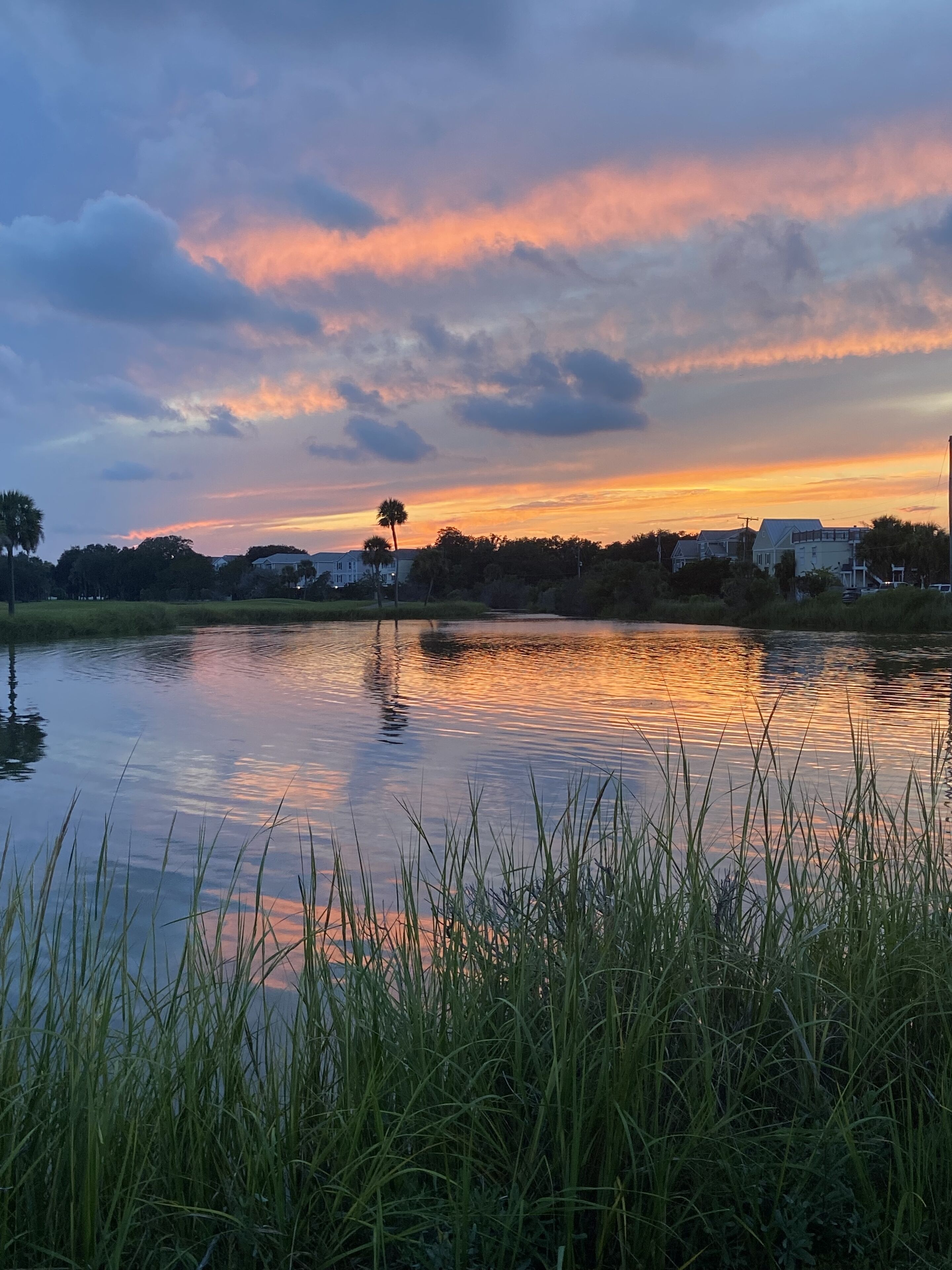 Un lac paisible, avec un coucher de soleil en arrière-plan, entouré d’herbe et d’arbres.