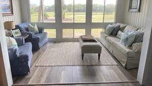 Ein Wohnzimmer mit zwei Sofas, einem Couchtisch und einem Teppich. Große Fenster bieten Blick auf einen Golfplatz.