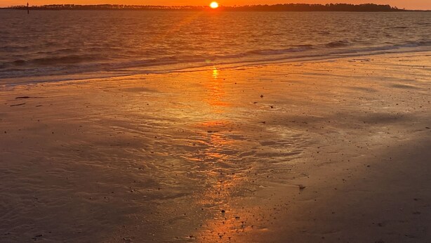 Ein Sonnenuntergang über einem Strand mit ruhigem Wasser, das den Himmel spiegelt.