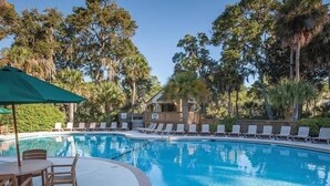 Ein Swimmingpool mit Liegestühlen und einem Tisch, umgeben von Bäumen und einem Holzgebäude.