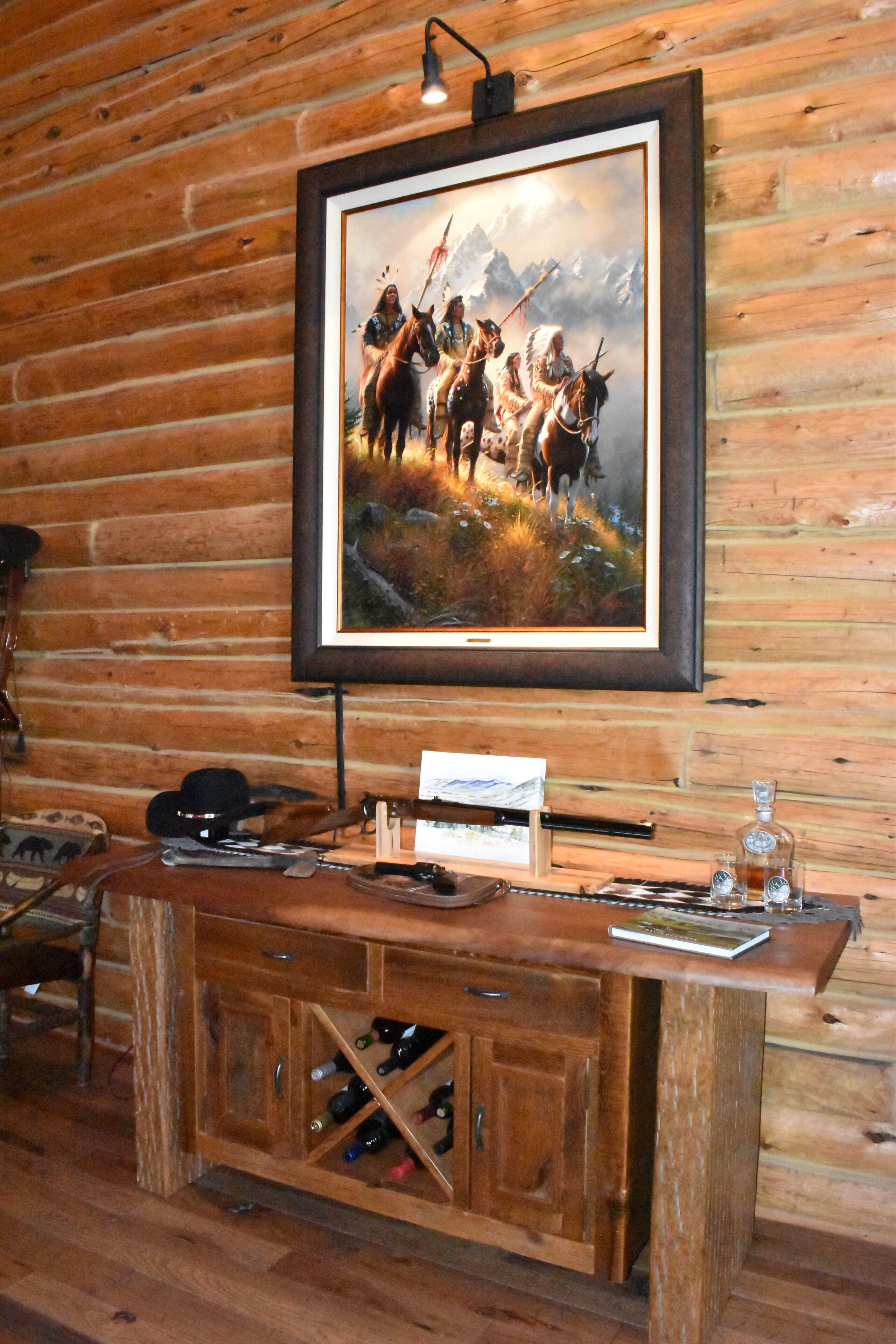 Een houten cabin interieur met een schilderij van een berglandschap, een houten bar met flessen en een rustieke houten vloer.