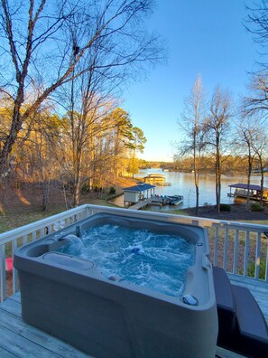 A hot tub on a deck with a view of a lake and dock.