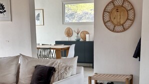 Olohuone, jossa on valkoinen sohva, kuviollinen matto ja puinen kenkäteline.