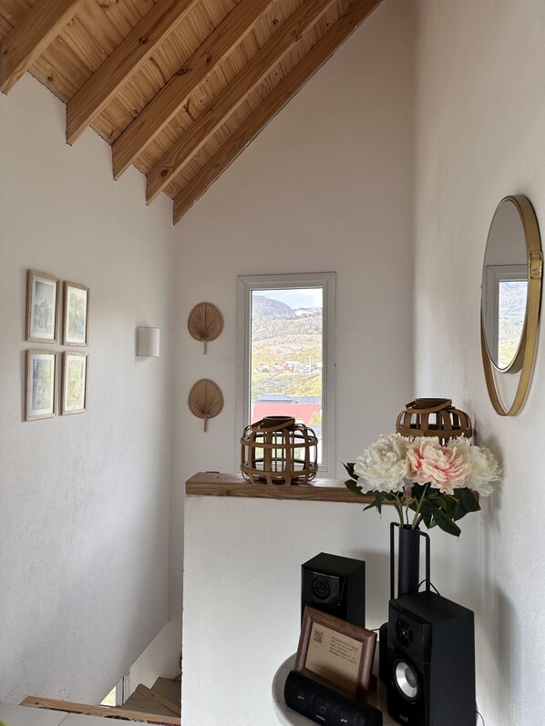 Ein Zimmer mit Holzboden, einem Fenster mit Bergblick, einem Spiegel, gerahmten Bildern und einem Lautsprecher.